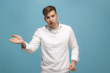 Image showing Beautiful male half-length portrait isolated on blue studio backgroud. The young emotional surprised man