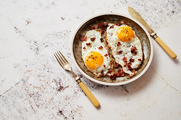 Image showing Two fresh fried eggs with crunchy crisp bacon served on rustic plate