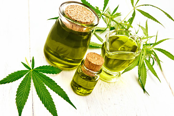 Image showing Oil hemp in gravy boat and two jars on wooden board