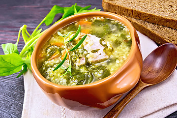 Image showing Soup with couscous and spinach in clay bowl on wooden board