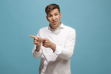 Image showing Beautiful male half-length portrait isolated on blue studio backgroud. The young emotional surprised man