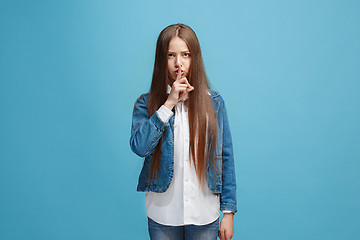 Image showing The young teen girl whispering a secret behind her hand over blue background