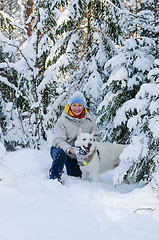 Image showing Joyful woman with a white dog in the winter snow-covered forest