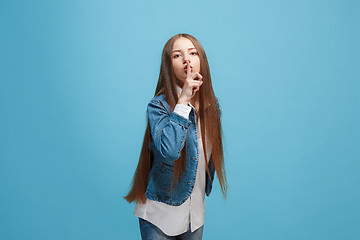 Image showing The young teen girl whispering a secret behind her hand over blue background