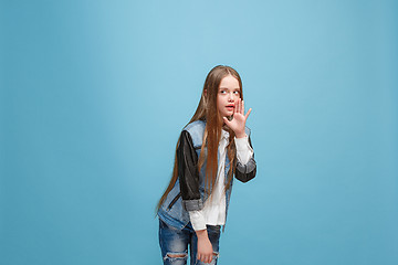 Image showing The young teen girl whispering a secret behind her hand over blue background