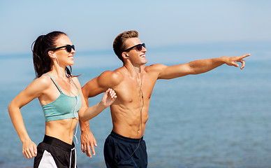 Image showing couple with earphones running along on beach