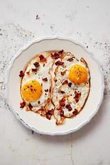Image showing Two fresh fried eggs with crunchy crisp bacon and chive served on rustic plate