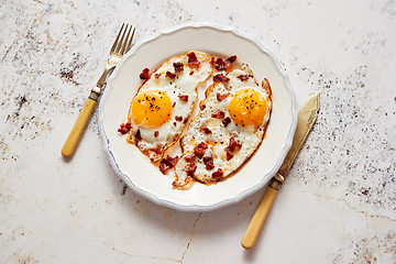 Image showing Two fresh fried eggs with crunchy crisp bacon and chive served on rustic plate