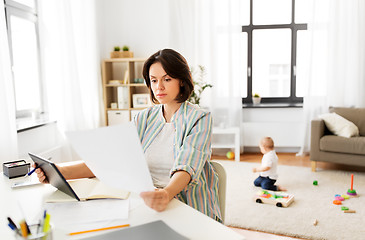 Image showing working mother with tablet pc and papers at home