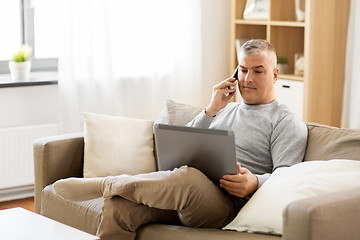 Image showing man with laptop calling on smartphone at home