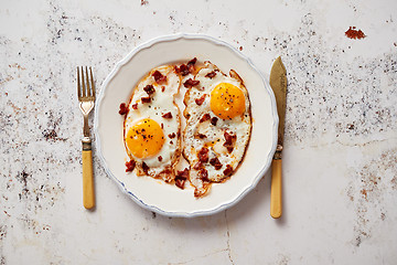 Image showing Two fresh fried eggs with crunchy crisp bacon and chive served on rustic plate