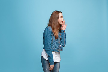 Image showing The young teen girl whispering a secret behind her hand over blue background