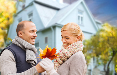 Image showing smiling couple with autumn maple leaves over house