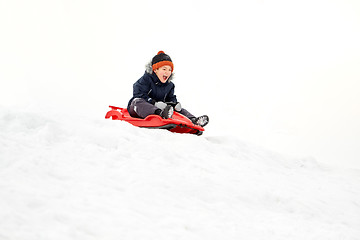 Image showing happy boy sliding on sled down snow hill in winter