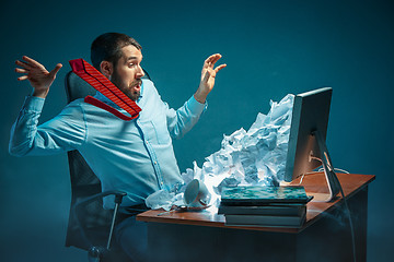 Image showing Young stressed handsome businessman working at desk in modern office shouting at laptop screen and being angry about spam