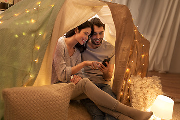 Image showing happy couple with smartphone in kids tent at home