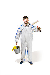 Image showing Young male decorator painting with a paint roller climbed a ladder isolated on white background.