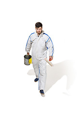 Image showing Young male decorator painting with a paint roller climbed a ladder isolated on white background.