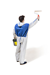 Image showing Young male decorator painting with a paint roller climbed a ladder isolated on white background.