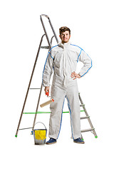 Image showing Young male decorator painting with a paint roller climbed a ladder isolated on white background.