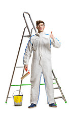 Image showing Young male decorator painting with a paint roller climbed a ladder isolated on white background.