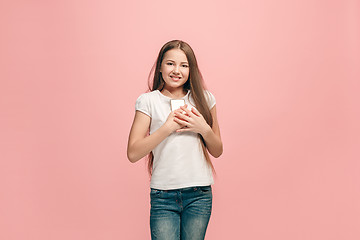 Image showing The happy teen girl with phone standing and smiling against pink background.