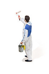 Image showing Young male decorator painting with a paint roller climbed a ladder isolated on white background.