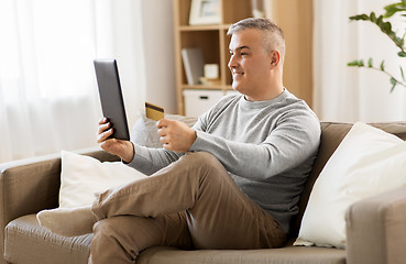 Image showing man with tablet pc and credit card on sofa at home