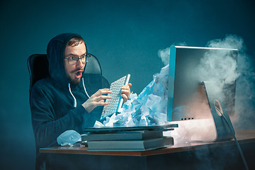 Image showing Young stressed handsome businessman working at desk in modern office shouting at laptop screen and being angry about spam