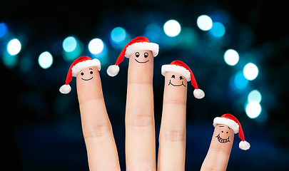 Image showing close up of four fingers in santa hats over lights