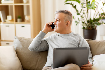 Image showing man with laptop calling on smartphone at home