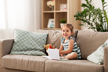 Image showing happy girl sitting on sofa with book at home