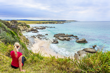 Image showing Female sitting by the coastal bluff looking out to the rocky beach belo