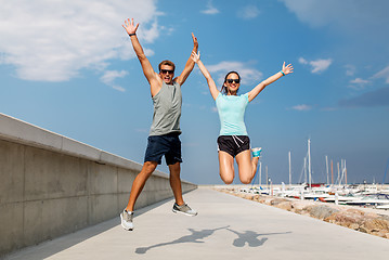 Image showing happy couple in sports clothes jumping on pier