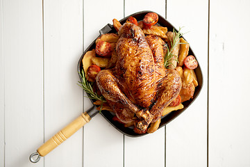 Image showing Grilled whole chicken in cast iron black pan with potatoes, tomatos and rosemary