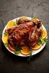 Image showing Roasted whole chicken or turkey served in white ceramic plate with oranges