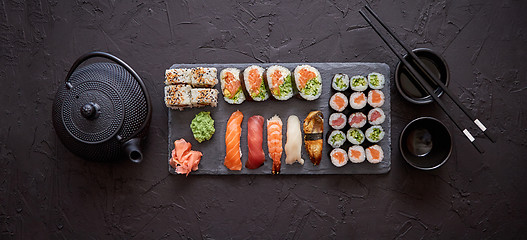 Image showing Assortment of different kinds of sushi rolls placed on black stone board