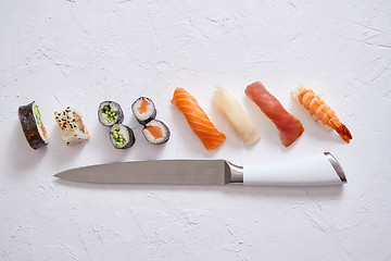 Image showing Various sushi rolls with Japanese knife on white stone slate background