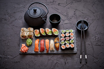 Image showing Assortment of different kinds of sushi rolls placed on black stone board