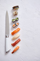 Image showing Various sushi rolls with Japanese knife on white stone slate background