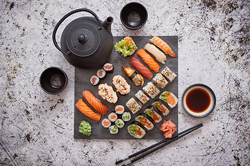 Image showing Assortment of different kinds of sushi rolls placed on black stone board