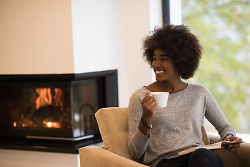 Image showing black woman reading book  in front of fireplace