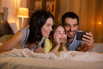 Image showing happy family with smartphone in bed at night