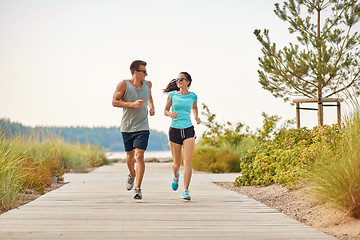 Image showing couple in sports clothes running along beach path