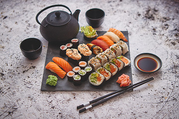 Image showing Assortment of different kinds of sushi rolls placed on black stone board