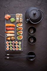 Image showing Assortment of different kinds of sushi rolls placed on black stone board