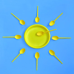 Image showing A yellow plastic plate and spoons lay around it on a bright blue background. The concept of a holiday, picnic.