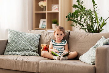 Image showing happy girl sitting on sofa with book at home