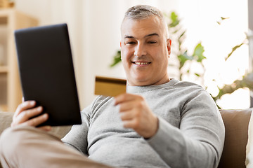 Image showing man with tablet pc and credit card on sofa at home