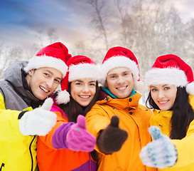 Image showing friends in santa hats showing thumbs up outdoors